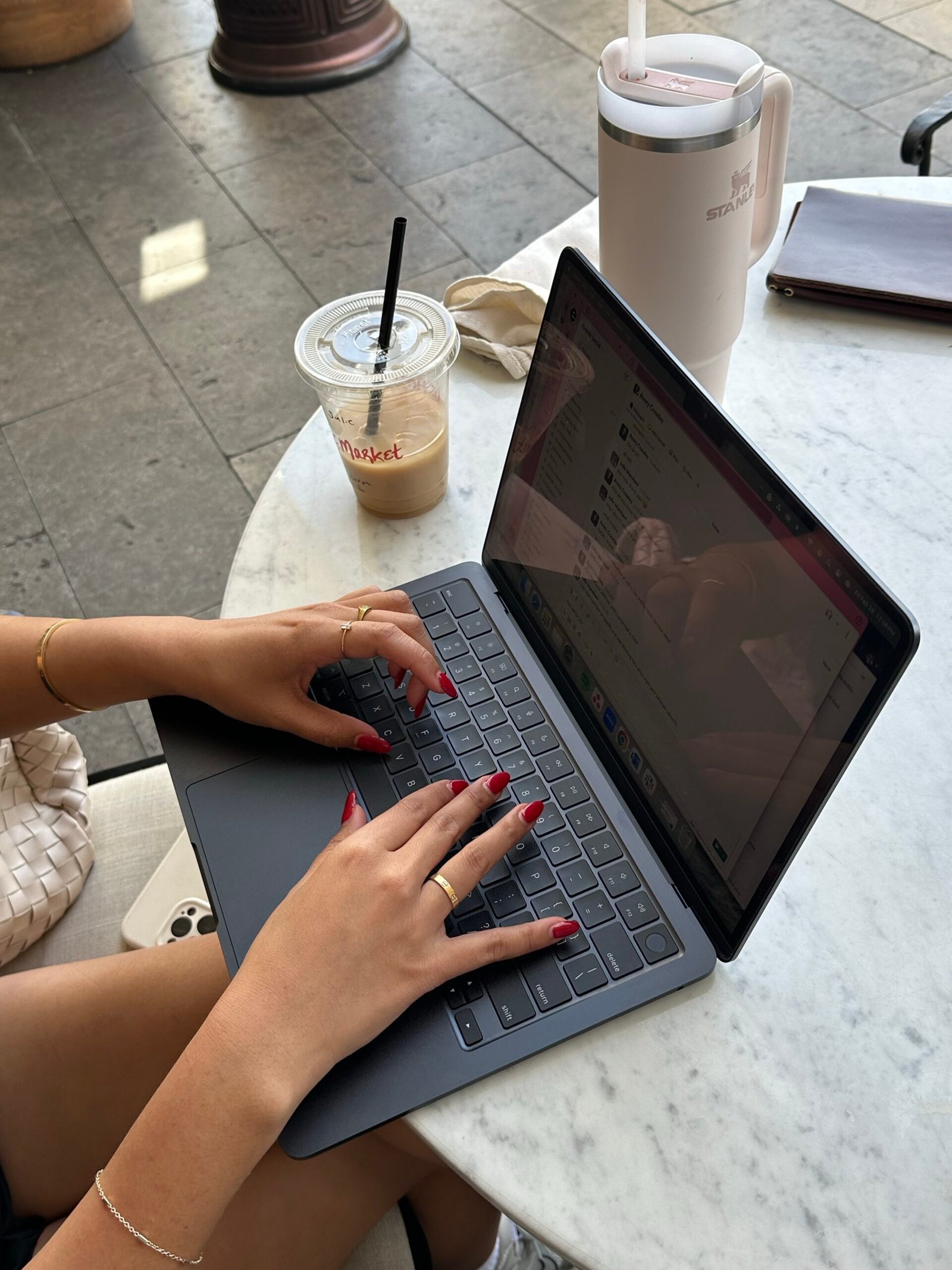 Person working on laptop at coffee shop with iced latte